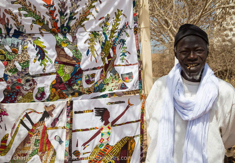 Fabric Artist Bara Fall and his Creations, Goree Island. He has a chewing stick in his mouth, for cleaning teeth.