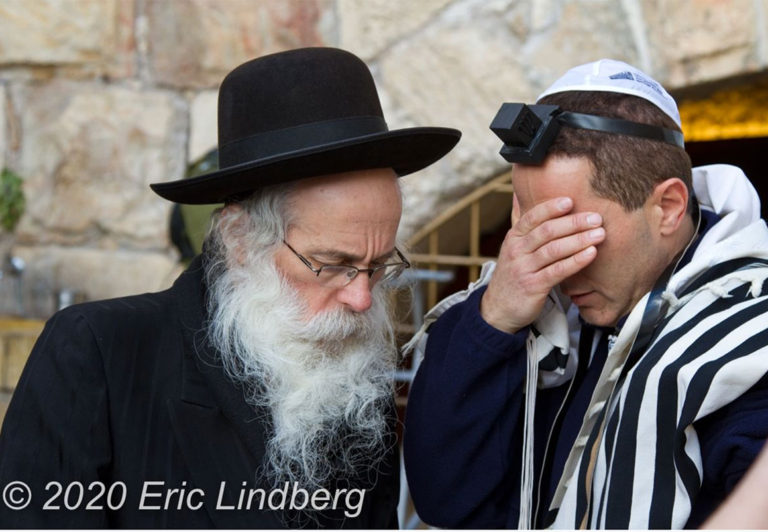 An Orthodox Jewish man instructs a visitor while reading verses from the Torah.