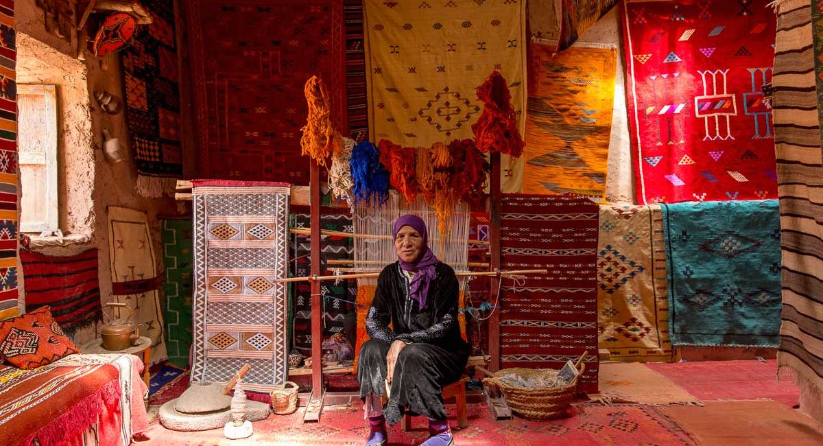 Rug weaver posing with colourful handwoven rugs in the Ait Benhaddou kasbah in Ouarzazate.