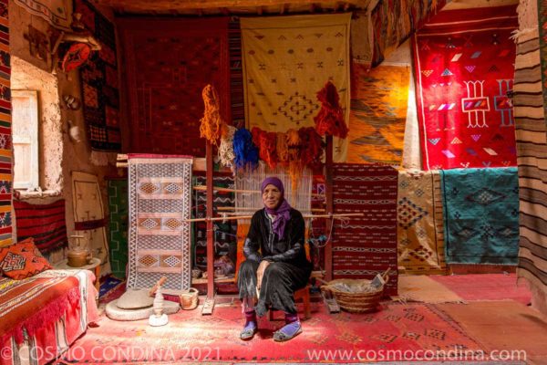 Rug weaver posing with colourful handwoven rugs in the Ait Benhaddou kasbah in Ouarzazate.