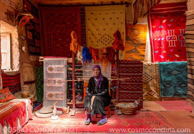 Rug weaver posing with colourful handwoven rugs in the Ait Benhaddou kasbah in Ouarzazate.