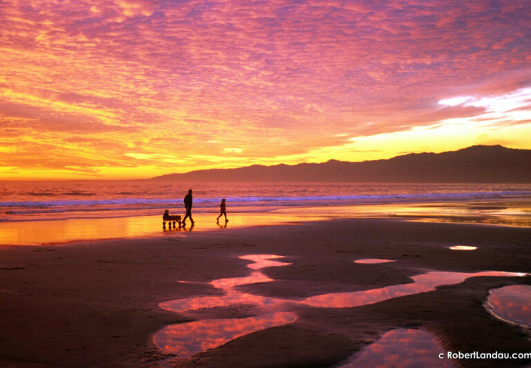 A father pulls his young child in a toy wagon across a peaceful stretch of beach just north of the Santa Monica Pier. The allure of open spaces, fresh air and Technicolor sunsets is hard to resist for newcomers and veteran photographers alike.