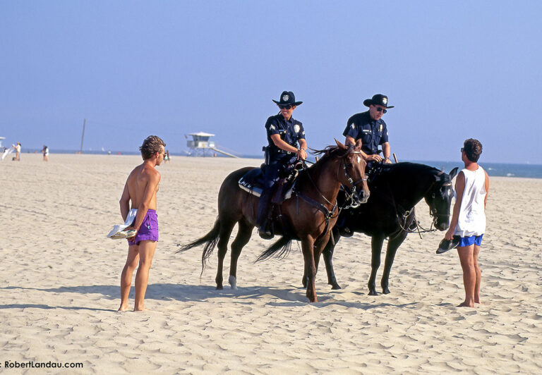 Police patrolling on horseback chat amiably with beach goers at Venice Beach.
