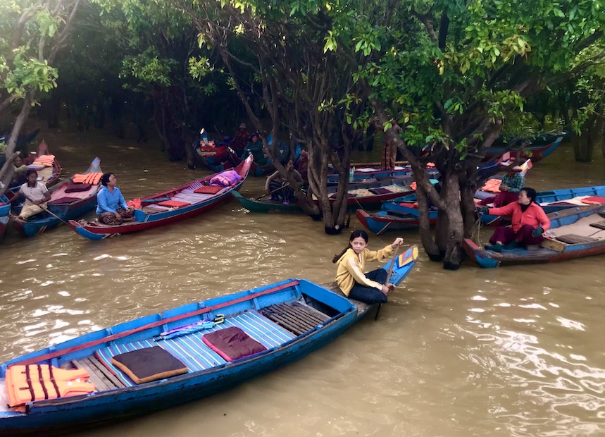 Khmer women paddle boats through the mangroves at the edge of the lake.