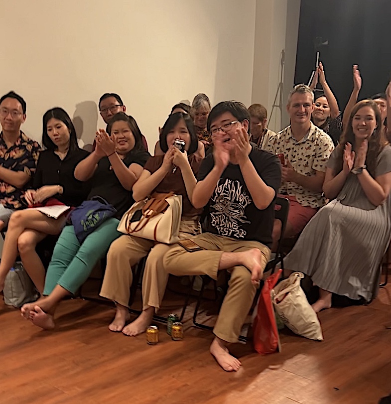 Part of a much larger audience in Singapore relaxes and gets comfortable while they watch their friends and relatives learn comedy skills at an improv workshop.