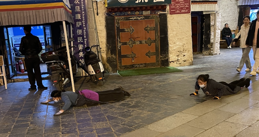 Tibetan Buddhist pilgrims prostrate themselves in prayer before rising to make their way slowly forward on Barkhor Street to Jokhang Temple, the most sacred pilgrimage destination in Tibet. 