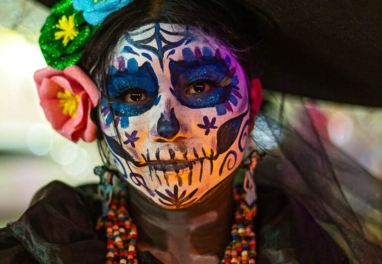 A lady costumed as La Calavera Catrina, an iconic figure popularized by artist Diego Rivers in his mural Sueño de una Tarde Dominical en la Alameda Central that sometimes appears in opposition to the Halloween Jack-o’-lantern.