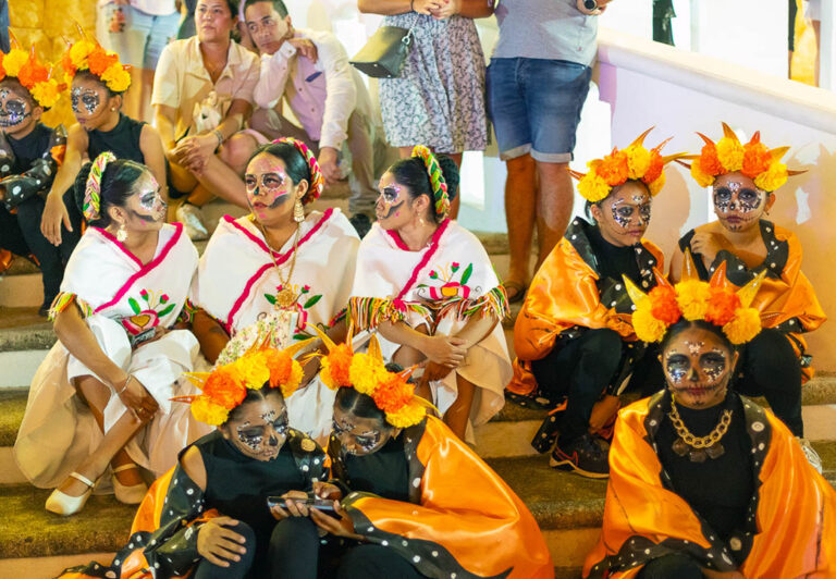 A group of teenagers dressed in Day of the Dead costumes rest on the steps of the main square after their on stage performance.