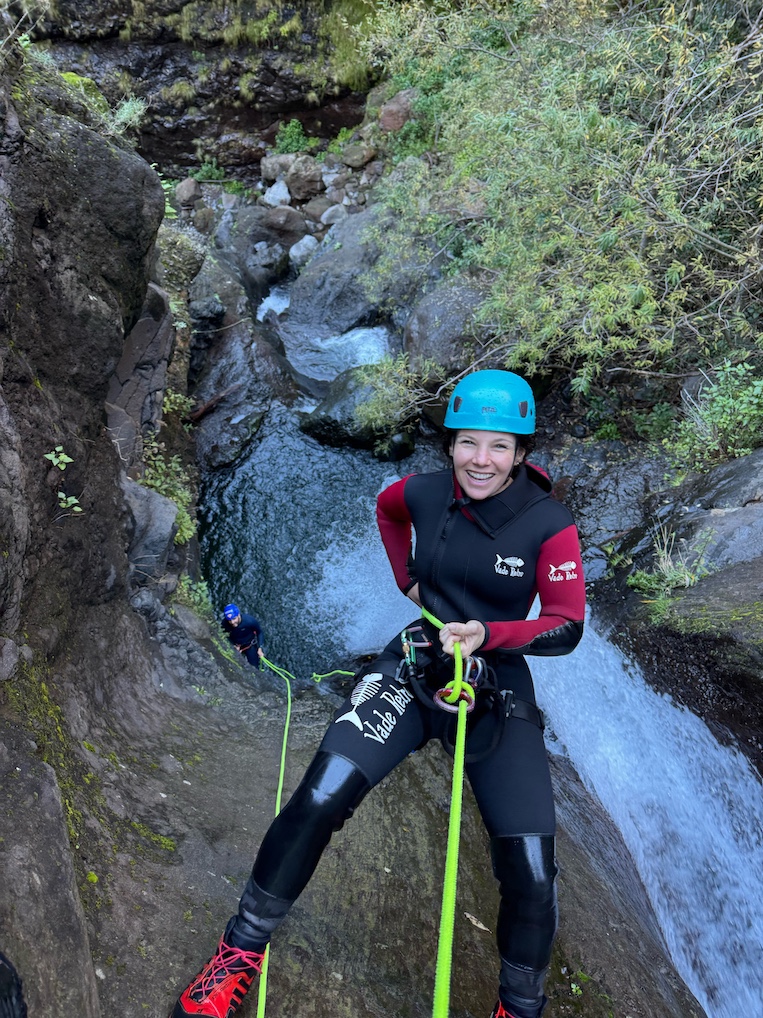 A woman rappels down a steep canyon wall.