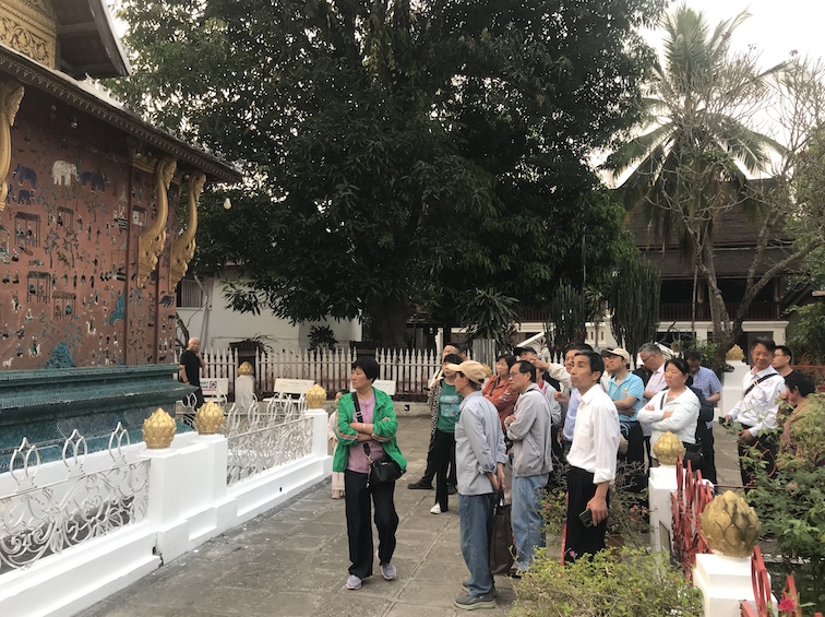 Chinese visitors listen to their tour guide describe the striking cut-glass mosaic work at Wat Xieng Thong.