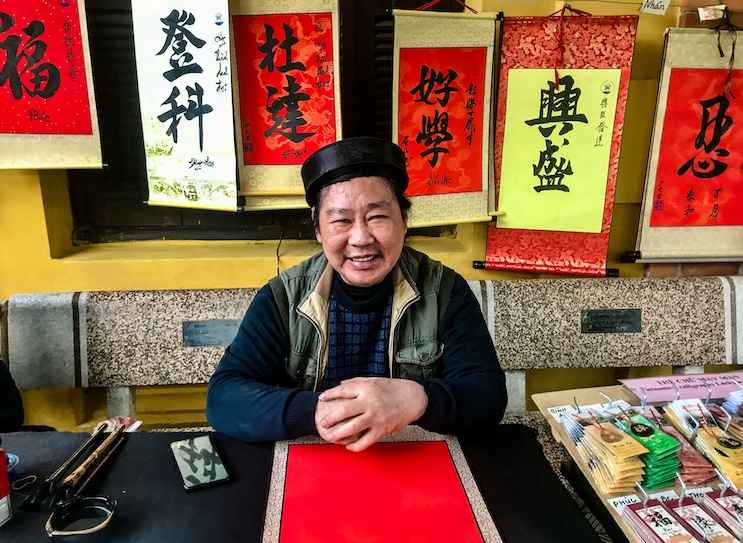 A calligrapher at the Ho Chi Minh Mausoleum Complex encourages visitors to purchase a hand-painted scroll bearing a Confucian mantra.